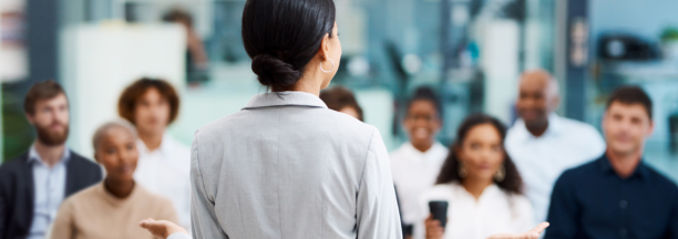 Back of woman as she speaks to a group of employees about benefits.