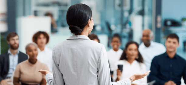 Back of woman as she speaks to a group of employees about benefits.