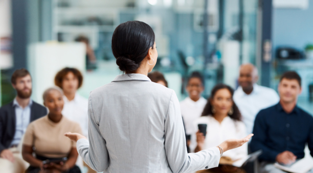 Back of woman as she speaks to a group of employees about benefits.